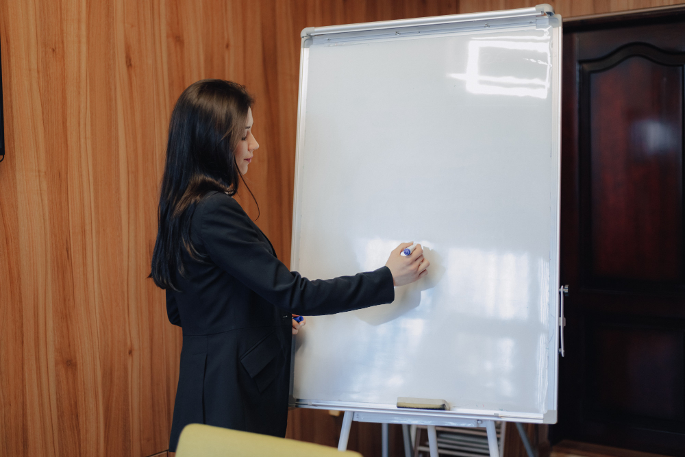 Woman in black suit writing on a blank whiteboard in office.