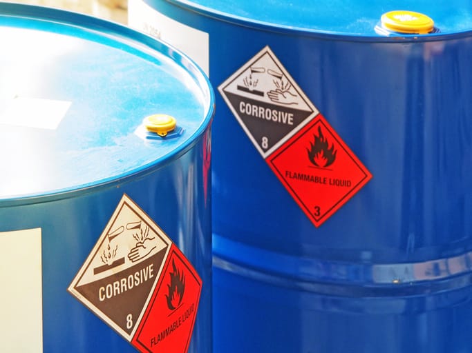Blue barrels with hazardous material labels for corrosive and flammable liquids.