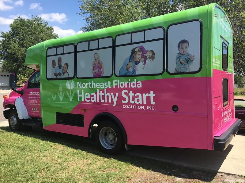 Bright green and pink bus with Northeast Florida Healthy Start Coalition graphics.