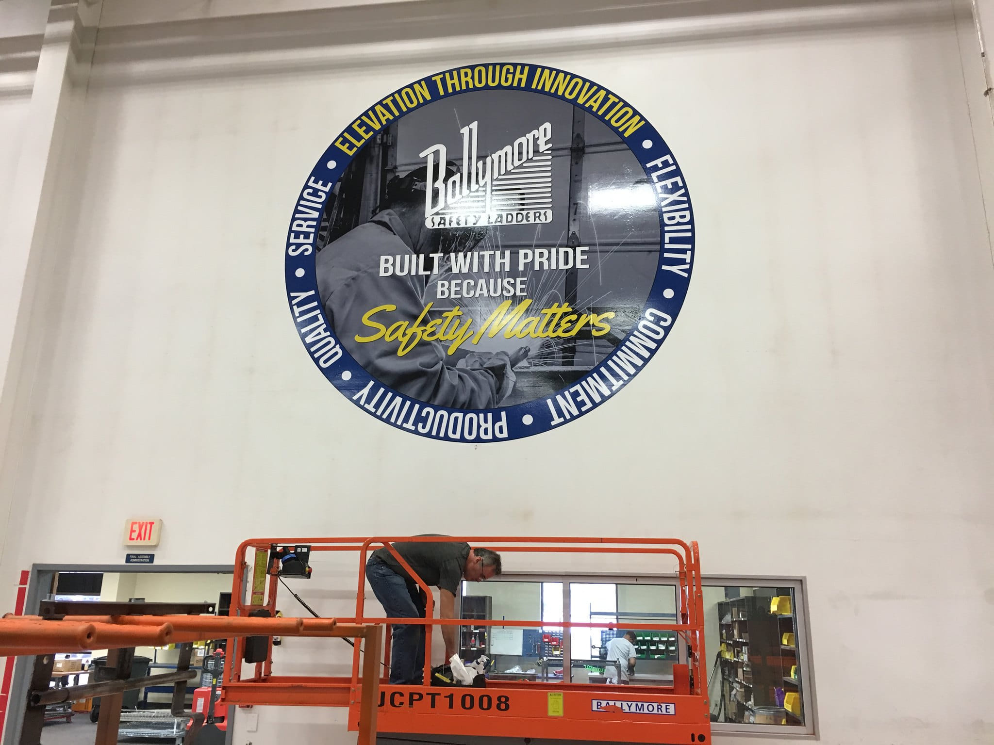 Large circular safety-themed wall graphic being installed in warehouse.