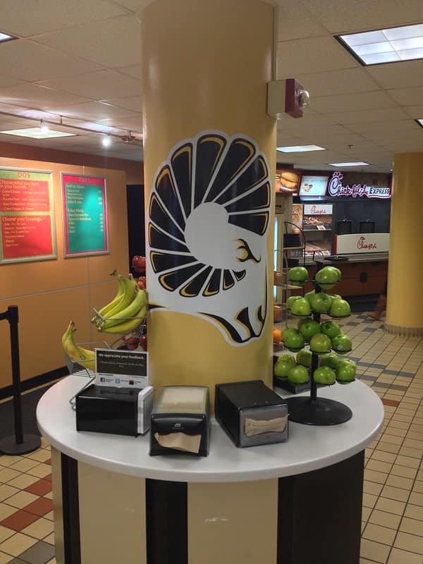 Cafeteria column with stylized lion logo beside fruit display station.